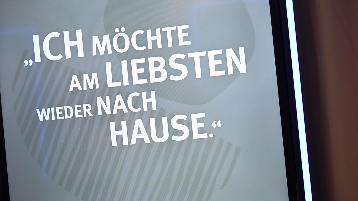 Ein graues Plakat auf dem in weißer Schrift steht: " Ich möchte am liebsten wieder nach Hause".