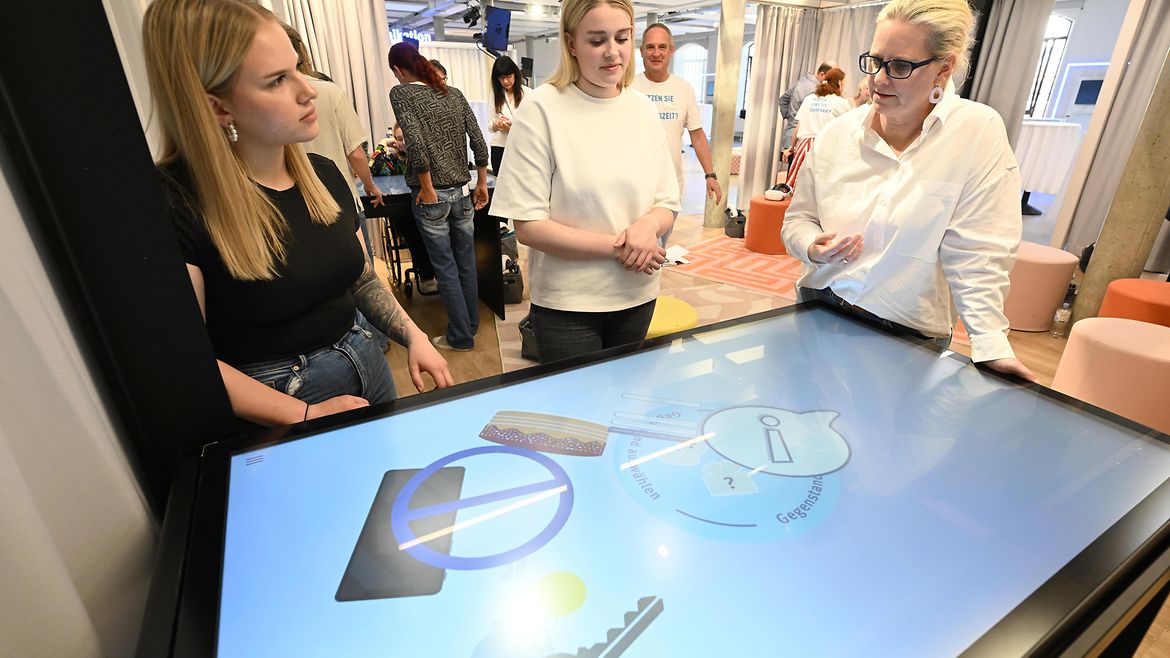 Drei Frauen stehen an einem Tisch mit Touchscreen