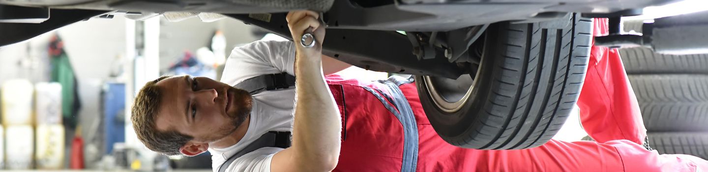 Ein Automechaniker repariert liegend ein Auto Ein Automechaniker repariert liegend ein Auto