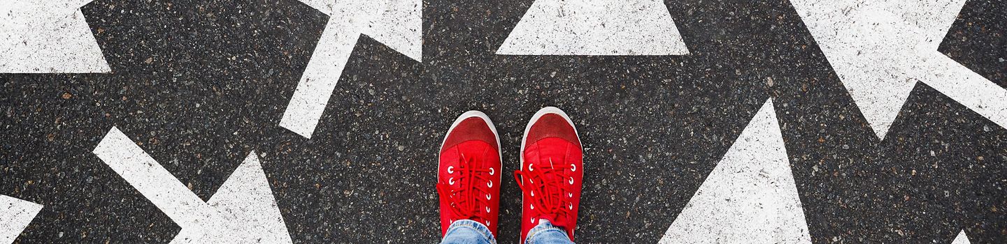 Füße in roten Schuhen von oben auf Asphalt, auf dem Pfeile in alle möglichen Richtungen