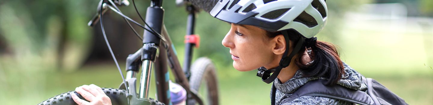 Frau mit Fahrradhelm prüft die Luft im Reifen an ihrem Fahrrad